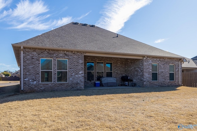 back of house featuring a shingled roof, brick siding, and a yard