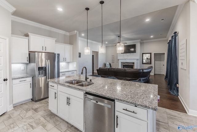 kitchen with a stone fireplace, a kitchen island with sink, a sink, open floor plan, and appliances with stainless steel finishes