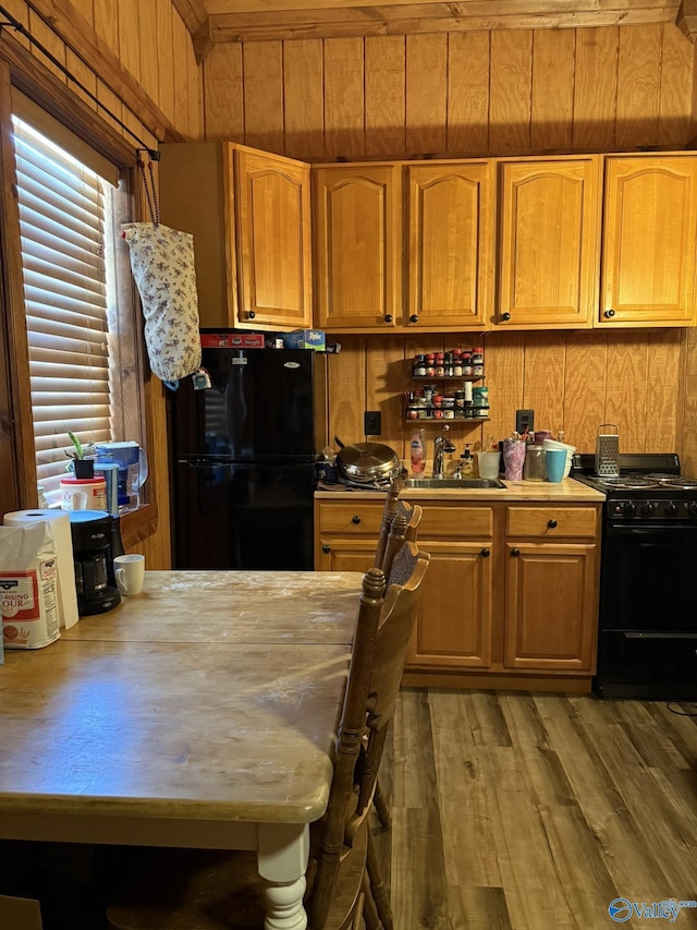 kitchen featuring black appliances, wood walls, a sink, and light countertops