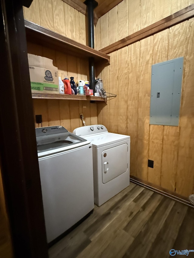 washroom featuring laundry area, electric panel, wooden walls, wood finished floors, and washing machine and dryer