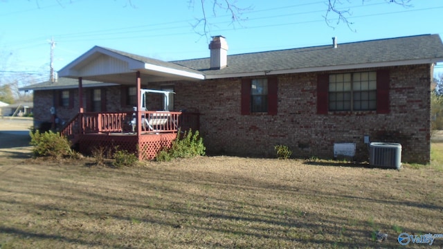 ranch-style house with brick siding, central AC unit, a chimney, a wooden deck, and a front yard