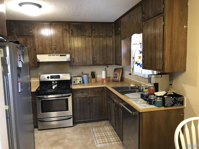 kitchen featuring stainless steel appliances, light countertops, a sink, dark brown cabinetry, and under cabinet range hood