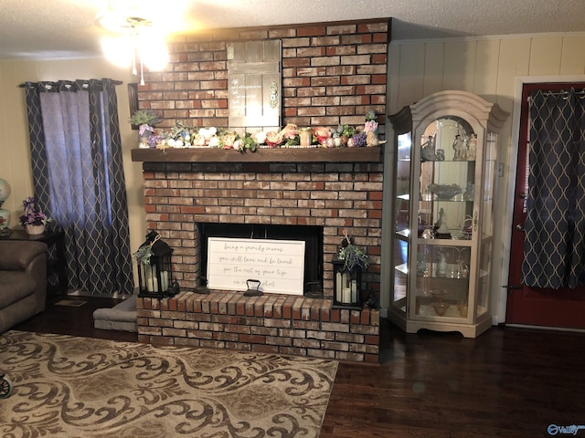 living room with a brick fireplace, a textured ceiling, and wood finished floors