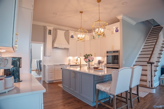 kitchen with a center island with sink, premium range hood, decorative light fixtures, dark hardwood / wood-style floors, and white cabinetry