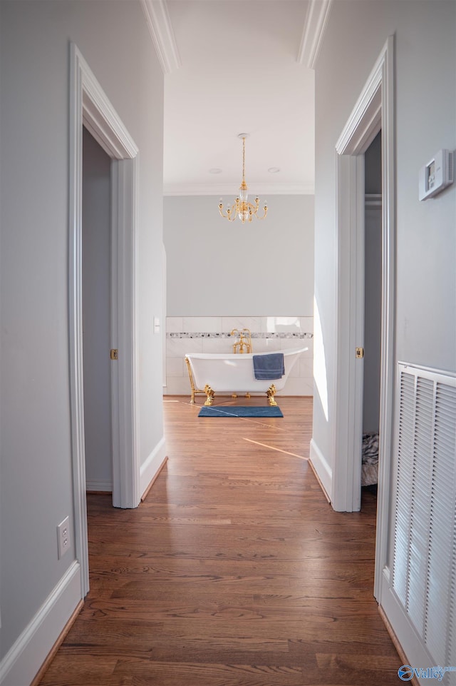 hallway with ornamental molding, a notable chandelier, and hardwood / wood-style flooring