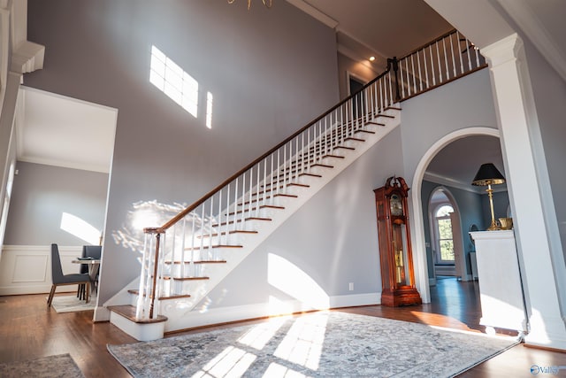 staircase with ornamental molding, wood-type flooring, and a towering ceiling