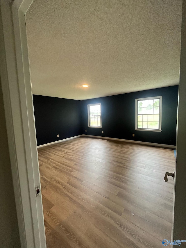 unfurnished room featuring baseboards, a textured ceiling, and wood finished floors