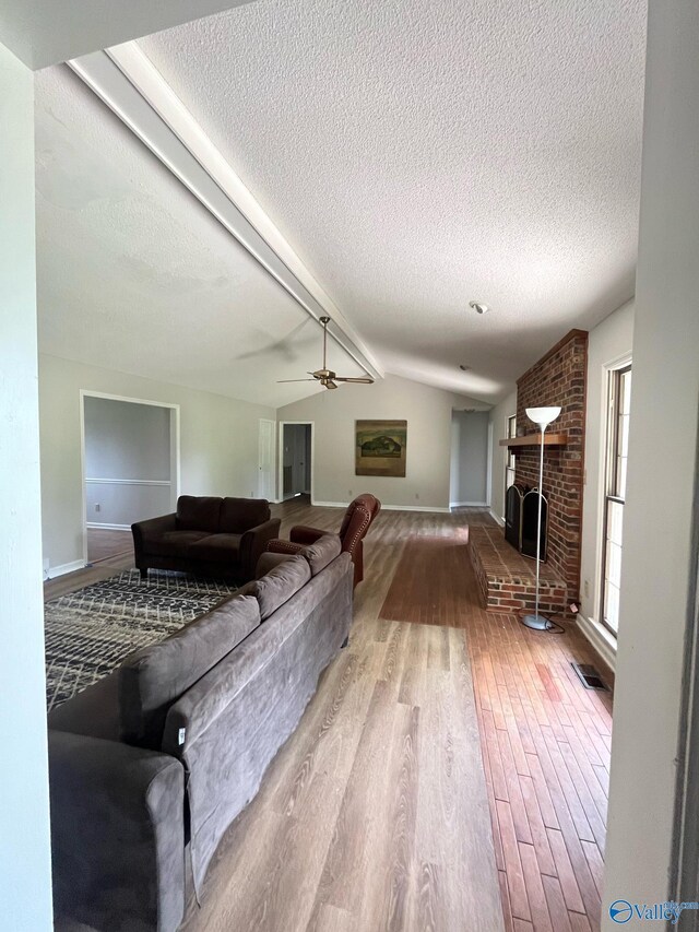 living room with vaulted ceiling with beams, a textured ceiling, a brick fireplace, and wood finished floors
