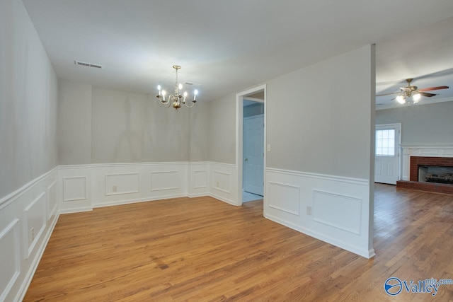 spare room featuring a fireplace, ceiling fan with notable chandelier, and light wood-type flooring