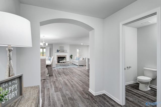 hall with dark wood-style floors, baseboards, visible vents, and arched walkways