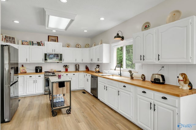 kitchen featuring a sink, decorative backsplash, black appliances, white cabinetry, and butcher block counters