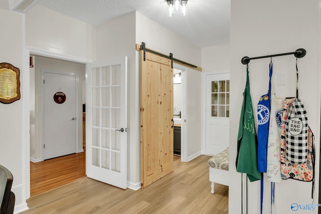 interior space featuring a textured ceiling, a barn door, light wood-type flooring, and baseboards