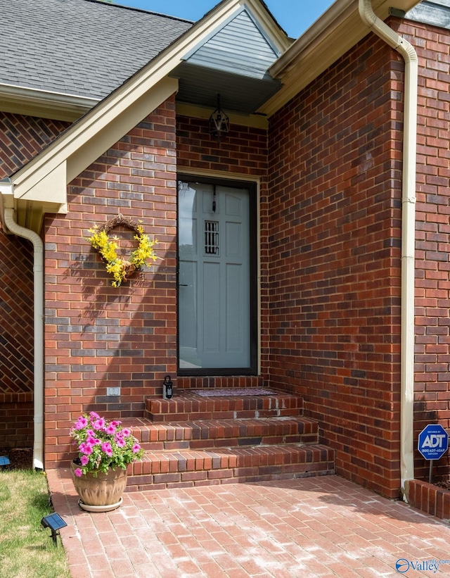 view of exterior entry with roof with shingles and brick siding