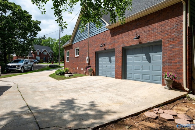 view of side of home with concrete driveway, a shingled roof, an attached garage, and brick siding