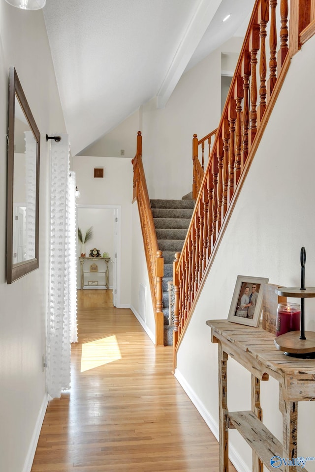 stairway with baseboards, visible vents, wood finished floors, and lofted ceiling