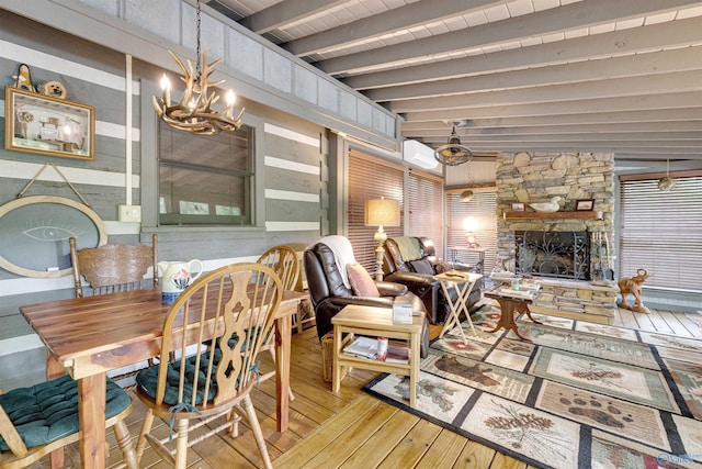 interior space with a stone fireplace, a notable chandelier, beamed ceiling, a wall mounted air conditioner, and light hardwood / wood-style flooring