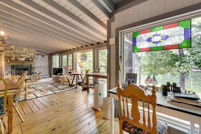 sunroom / solarium with a stone fireplace and lofted ceiling with beams