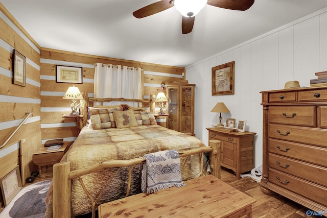 bedroom with hardwood / wood-style floors, ceiling fan, and wooden walls