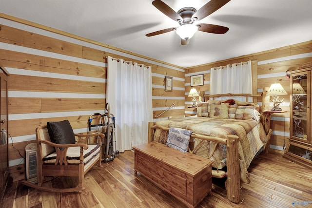 bedroom featuring ceiling fan, wood walls, and light hardwood / wood-style flooring