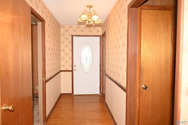 doorway featuring wallpapered walls, light wood finished floors, baseboards, a wainscoted wall, and an inviting chandelier