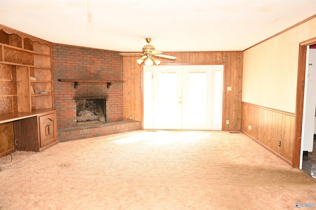 unfurnished living room with ornamental molding, a brick fireplace, carpet flooring, and wooden walls