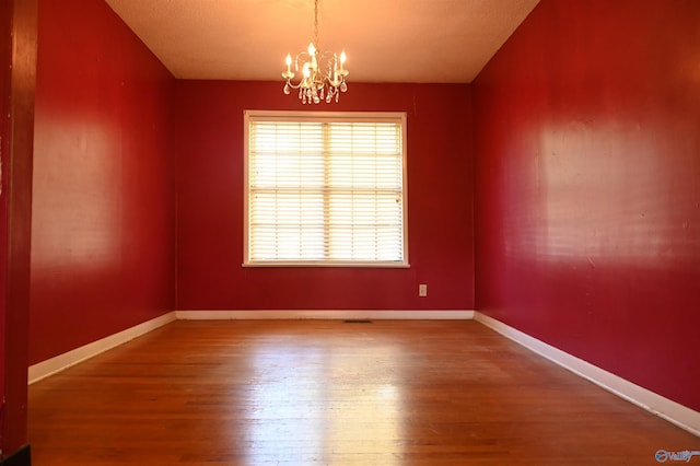 spare room featuring a chandelier, baseboards, and wood finished floors