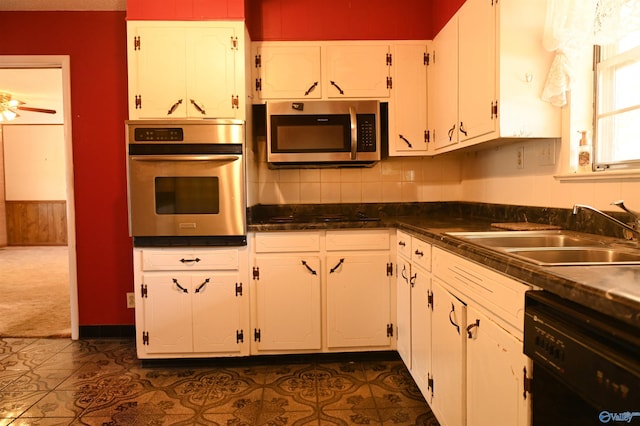 kitchen featuring stainless steel appliances, dark countertops, a sink, and white cabinets