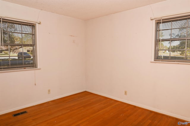 unfurnished room with baseboards, a textured ceiling, visible vents, and wood finished floors