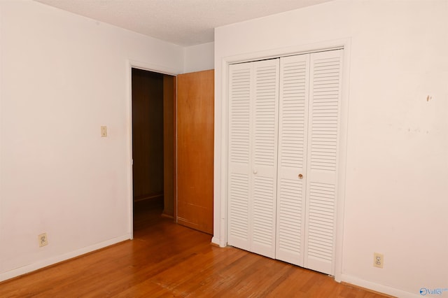 unfurnished bedroom featuring a textured ceiling, a closet, wood finished floors, and baseboards