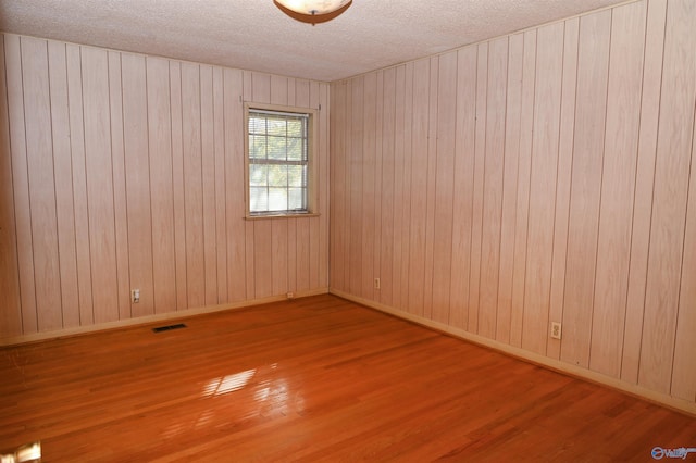 empty room with baseboards, a textured ceiling, visible vents, and wood finished floors