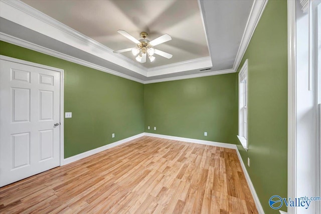 empty room with ceiling fan, light hardwood / wood-style floors, ornamental molding, and a tray ceiling