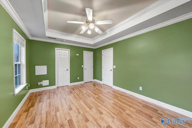 unfurnished room with light wood-type flooring, a tray ceiling, ceiling fan, and crown molding