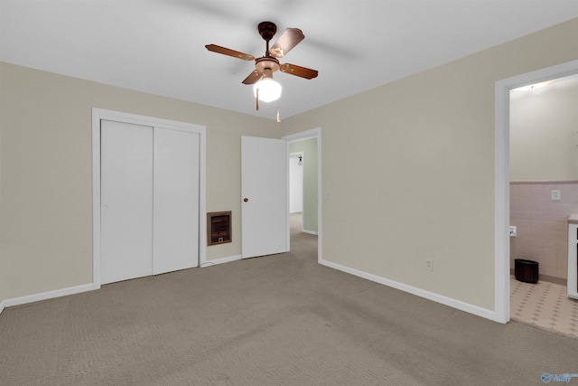 unfurnished bedroom with light carpet, heating unit, ceiling fan, connected bathroom, and a closet