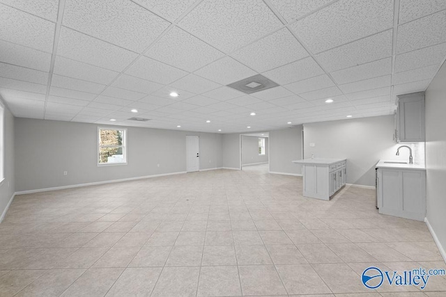 basement with a paneled ceiling, light tile patterned floors, and sink