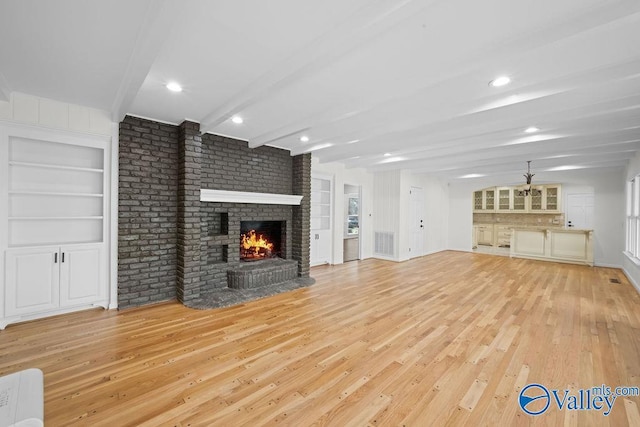 unfurnished living room featuring ceiling fan, light wood-type flooring, built in features, a fireplace, and beam ceiling