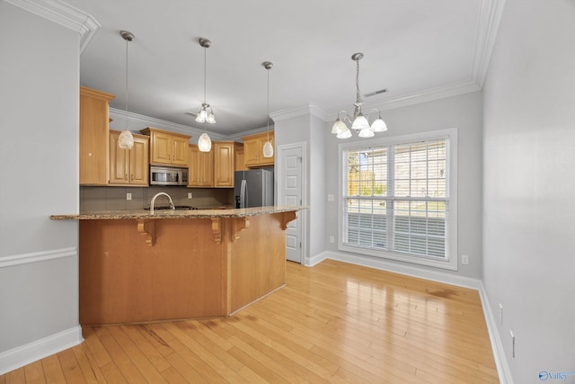 kitchen featuring stainless steel appliances, a chandelier, light wood-type flooring, a kitchen bar, and ornamental molding