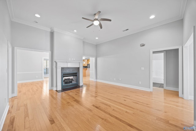 unfurnished living room with ceiling fan, ornamental molding, a towering ceiling, and light hardwood / wood-style flooring