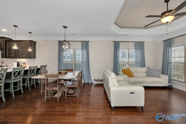 living room with ceiling fan with notable chandelier, ornamental molding, dark wood-type flooring, and a tray ceiling