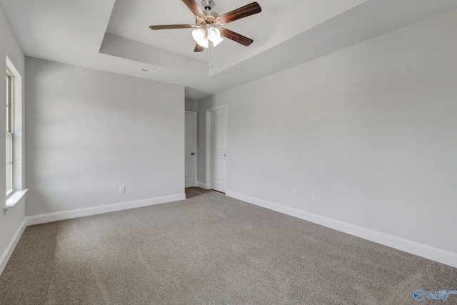 empty room featuring ceiling fan, a raised ceiling, and carpet floors