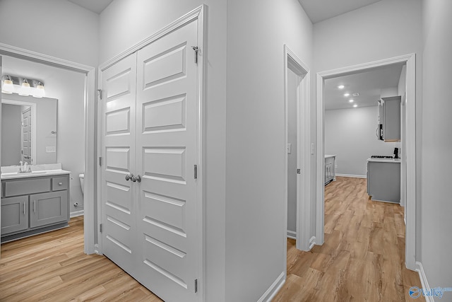 hallway featuring light wood-style flooring, baseboards, and a sink