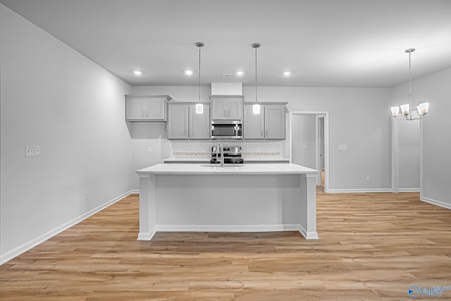 kitchen featuring light wood-type flooring, sink, decorative light fixtures, a center island with sink, and a chandelier