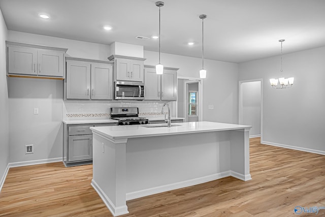 kitchen with pendant lighting, light countertops, appliances with stainless steel finishes, a kitchen island with sink, and a sink