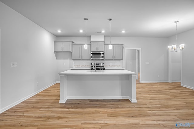 kitchen featuring a sink, light countertops, hanging light fixtures, stainless steel microwave, and an island with sink