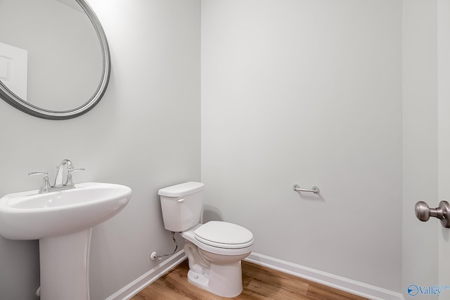 half bath with a sink, wood finished floors, toilet, and baseboards