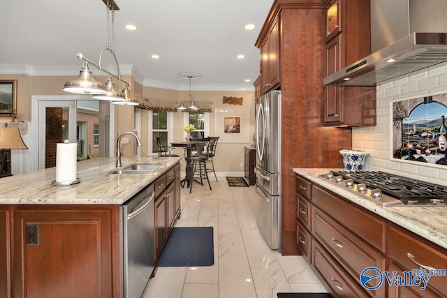 kitchen with appliances with stainless steel finishes, wall chimney exhaust hood, pendant lighting, a kitchen island with sink, and sink