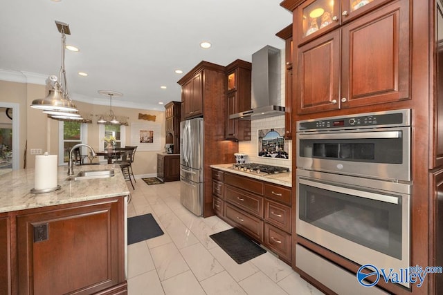 kitchen with pendant lighting, sink, wall chimney exhaust hood, stainless steel appliances, and ornamental molding