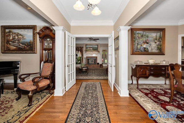 entryway featuring ceiling fan with notable chandelier, a brick fireplace, decorative columns, and hardwood / wood-style floors