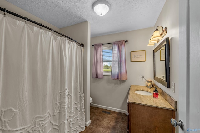 full bathroom featuring toilet, vanity, a textured ceiling, baseboards, and visible vents
