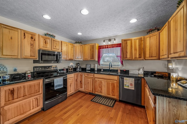 kitchen featuring a sink, light wood finished floors, stainless steel appliances, recessed lighting, and dark stone counters