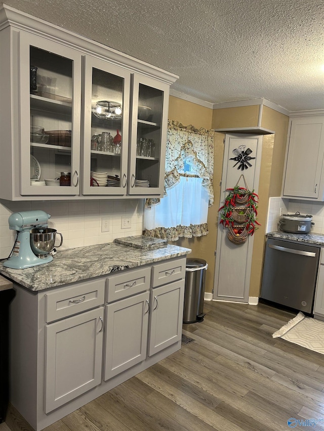 kitchen featuring tasteful backsplash, dishwasher, dark hardwood / wood-style flooring, crown molding, and light stone countertops